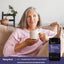 Woman on couch holding a mug next to a jar of Relaxing Sleep Powder.