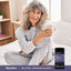 Woman in pajamas relaxes with a mug beside a Melatonin + Magnesium Glycinate bottle.