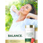 A woman smiles at the sun outdoors, holding a Carlyle Cayenne Complex 600 mg bottle.