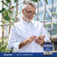 An elderly man uses a smartphone next to an Acetyl L-Carnitine HCL supplement bottle.