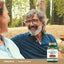 Older man and woman smiling and laughing outdoors, with an Arjuna Extract bottle in the bottom right corner.