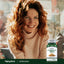 A young woman with red curly hair smiles beside a bottle of Astragalus in a lifestyle setting.