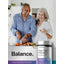 Older man chopping vegetables and woman smiling with a glass in a kitchen, featuring Triple Fiber + Probiotics bottle.
