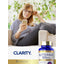 Middle-aged woman smiling at her phone on a couch, next to a Butterbur bottle.