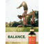 Two young adults perform an acroyoga pose in a sunny park with a Carlyle Potent Hemp Oil bottle.