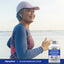 An older woman jogging on a beach, holding a bottle of Calcium Magnesium Citrate.