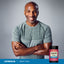 Middle-aged Black man in a gray athletic shirt smiling with arms crossed next to a CoQ10 jar.