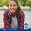 A middle-aged woman smiles outdoors next to a bottle of Colloidal Minerals.