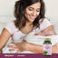 A young woman smiles warmly while holding a baby, with a Fenugreek bottle visible in the foreground.