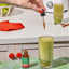 Woman's hand adds liquid to a green smoothie, with a bottle of Lions Mane Liquid Coffee on the counter.