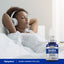Young woman relaxing in bed with headphones, next to a bottle of GABA, depicting a serene lifestyle moment.
