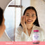 Young adult woman applying face cream while looking in a mirror, next to a bottle of Hair, Skin & Nails supplement.