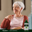 An older woman sits smiling, holding reading glasses next to a bottle of Liquid Chlorophyll.