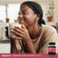 Smiling young woman holds a mug and a bottle of Magnesium Gummies, showcasing a healthy lifestyle.