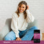 Young woman smiling in an armchair with a bottle of Multi Collagen Peptides beside her.