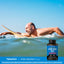 A middle-aged man smiles while paddling a surfboard in the ocean with a bottle of Nitric Oxide Max.