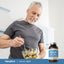 Older man smiling as he stirs a salad with a fork, next to a bottle of Fish Oil, highlighting a healthy lifestyle.