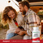 Young couple sitting in a car trunk, laughing and holding hands, with a One Daily Essential Multivitamin bottle.