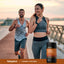 Two adults jogging on a waterfront path, with a Piping Rock Turmeric Curcumin Complex 800 mg bottle nearby