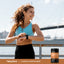 Woman in athletic wear checking her smartwatch outdoors with Piping Rock Vitamin B1 Benfotiamine 300mg bottle nearby