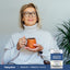 Adult holding a mug while smiling, with a Piping Rock Daily Fiber Probiotic + Prebiotic Powder bottle nearby
