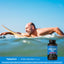 Middle-aged man paddles a surfboard in the ocean, smiling, with a Nitric Oxide Max bottle beside him.