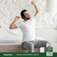 Adult stretching while sitting on the edge of a bed, with a Piping Rock Mucuna Ashwagandha Complex supplement bottle nearby