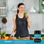 Adult standing in a kitchen holding a glass of green smoothie and a Piping Rock Ultimate Probiotic 100 Billion CFU bottle, 27 Probiotic Strains with Prebiotics, Daily Digestive Balance, 60 delayed release vegan capsules.