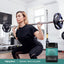 Adult performing a barbell squat in a gym, with a Piping Rock Creatine + Multi Collagen powder bottle nearby