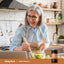 Adult preparing a salad in a kitchen with a Piping Rock NMN Complex with Resveratrol 500 mg & Collagen bottle nearby.