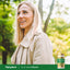 An adult woman smiles outdoors next to a bottle of Oil of Wild Oregano.