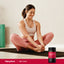A young woman stretches on a yoga mat next to a Beet Root bottle, reflecting a healthy lifestyle scene.