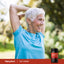 An older woman smiling and stretching outdoors with a bottle of Tart Cherry extract.