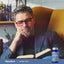 A man with grey hair and glasses is reading a book next to a Lutein + Zeaxanthin supplement bottle.