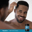 A young man examines his hair in a mirror beside a DHT Hair Formula bottle.