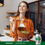 Lifestyle image of an adult holding a bowl of salad and a fork in a kitchen with a Piping Rock Magnesium Oxide 500 mg supplement bottle displayed in the bottom right corner