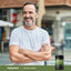 Middle-aged man smiling, arms crossed, standing next to a bottle of Chanca Piedra.