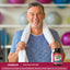 Middle-aged man smiling post-workout, towel around neck, holding Prostate Support bottle.