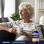 Elderly woman smiling while relaxing and holding a mug, with a bottle of Quercetin & Bromelain beside her.