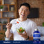 An adult man happily eats a salad with a bottle of R-Lipoic Acid, smiling at the camera.