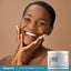Young adult Black woman smiling, hands cupping her face, beside a Retinol Gel Cream jar.