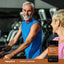 Older man and woman exercising in a gym with a bottle of Turmeric Curcumin CoQ10 Astaxanthin displayed nearby.