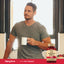 A man in his 30s stands in a kitchen holding a mug beside an Ultra Nattokinase bottle.