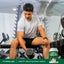 Young adult male performs bicep curls on a gym bench next to a tub of WheyFit Isolate Natural Vanilla.
