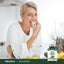 An older woman smiles while eating an apple next to a bottle of Wild Lettuce.